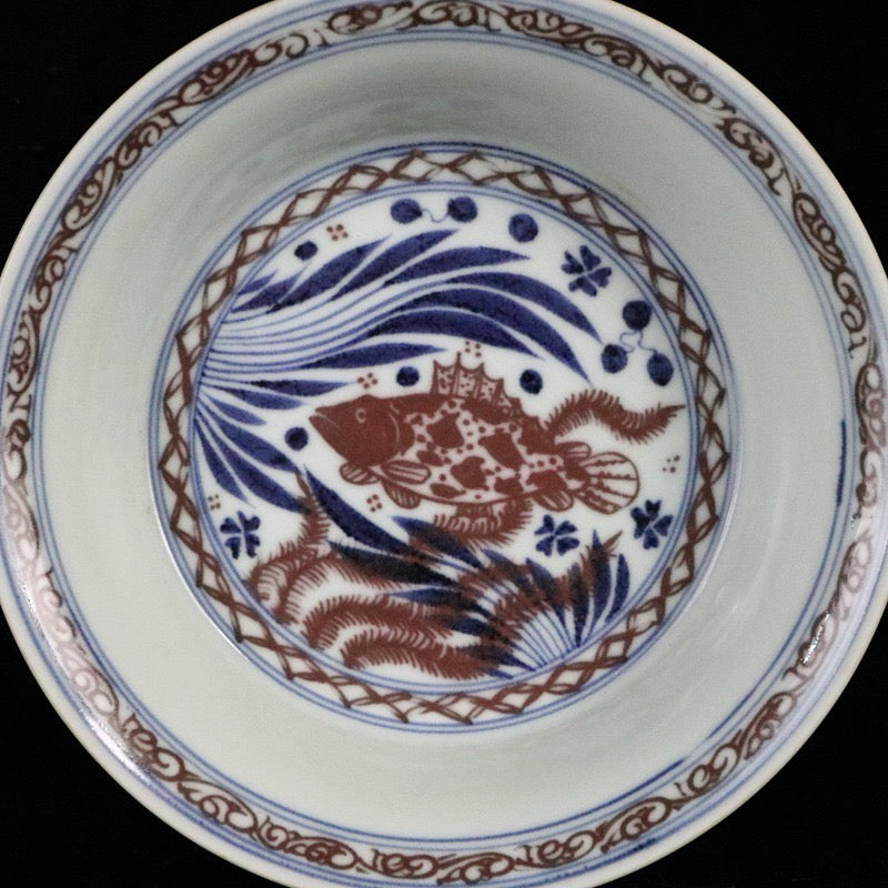 Blue and white glazed dish with red fish and algae patterns